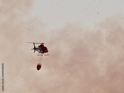 Aerial Firefighting Helicopter with Water Bucket in Smoky Sky