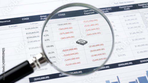 Magnifying glass focusing on red financial numbers on a paper spreadsheet