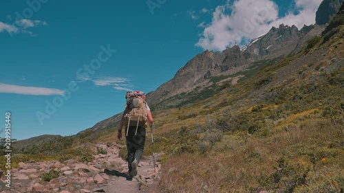 Following behind a backpacking hiker on the Torres del Paine W Trek with mountains and blue skies, Patagonia, Chile