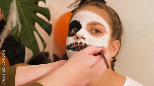 A cute teenage girl is getting ready for Halloween and doing face painting, with a skeleton painted on her face. October is a time of horror.