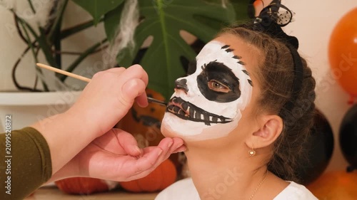 A cute teenage girl is getting ready for Halloween and doing face painting, with a skeleton painted on her face. October is a time of horror. makeup artist concept