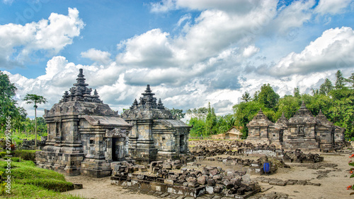 Bild auf Leinwand Ancient stone temples at Candi Kedulan archaeological site in Yogyakarta, Indonesia, surrounded by lush tropical landscape beneath dramatic clouds