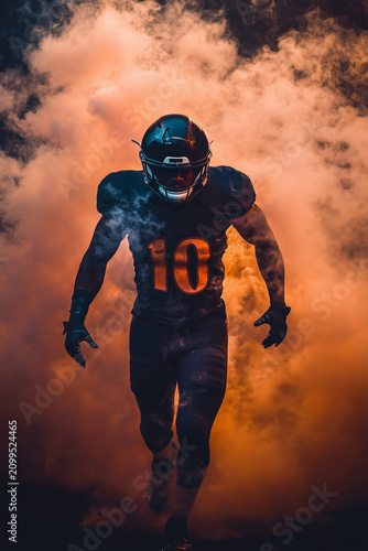 American football player emerging through dramatic orange smoke before a game