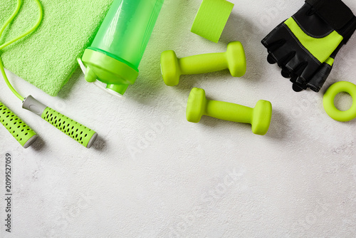 Green gym equipment and fitness accessories arranged at the top of a textured concrete background with empty space below. Flat lay.