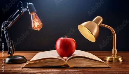 red apple on open book by vintage lamp on wooden desk