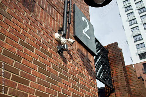Security camera installed on brick wall, in urban building exterior, with brick wall, security camera, number 2 sign, from a close-up perspective perspective, with brown, gray accents.