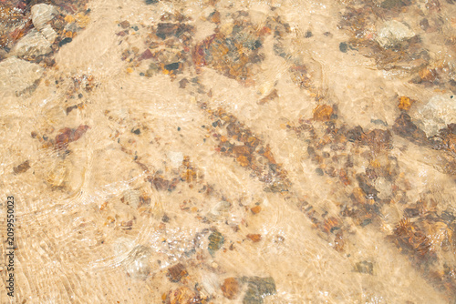 Quadro su tela Clear water flowing over a sandy riverbed with colorful pebbles and stones, crea