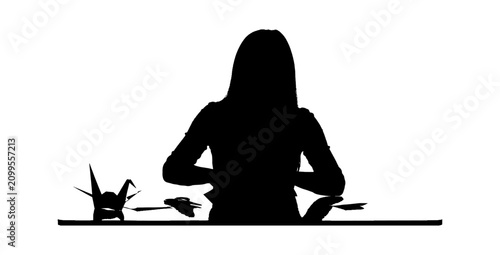 Black silhouette of a woman folding an origami paper crane at a desk Vector