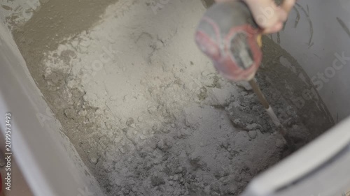 This close up video shows a mechanical paddler mixer attachment on a power drill mixing and blending dry mortar powder cement mix for a home renovation project.