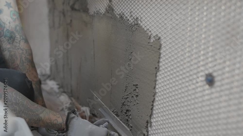 This video shows a construction worker carefully applying mortar to a metal lathe on a wall with a trowel.