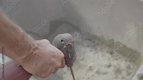 This POV video shows an overhead view of an electric drill mixer spinning and blending dry mortar powder in a bucket.
