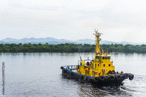 фотографія Harbor tugboat assisting a commercial vessel during port maneuvering with tropical mountains in the background at sunrise
