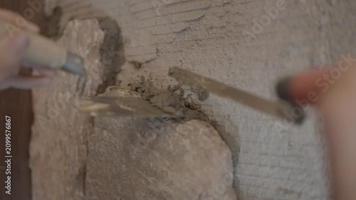 This video shows a close up of a specialty tool filling mortar gaps around a rock just placed by a mason on a rock wall.