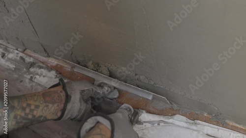 This video shows a mason with arm tattoos wearing protective gloves and using a steel trowel to flatten cement mortar on a wall.