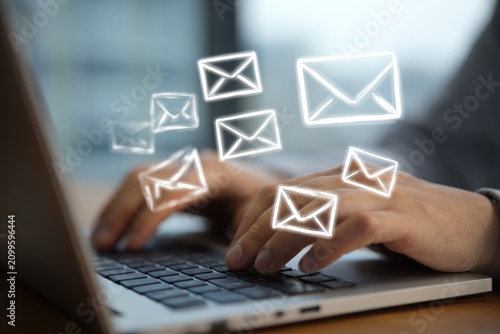 Close-up of hands typing on a laptop, with ethereal glowing email envelope icons floating above. Focus on technology