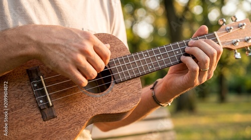Man playing ukulele outdoors in sunlight with bokeh background.