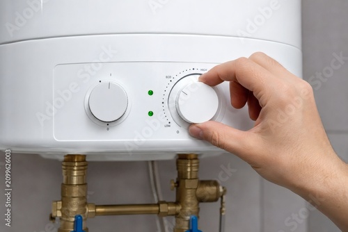 Adjusting Water Heater Temperature: A close-up shot shows a hand turning the knob on a white water heater, adjusting the temperature control to regulate hot water supply.