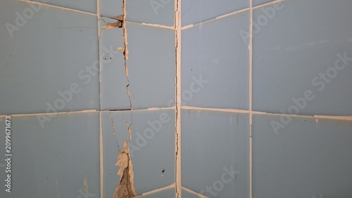 Cracked blue ceramic tile wall with structural damage corner