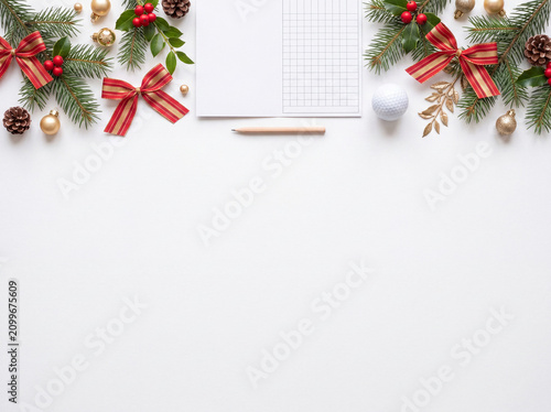 golf scorecard with a wooden pencil, white golf ball, pine branches, festive ribbon, holly berries, pinecones, and Christmas ornaments arranged neatly along the top edge of a clean white background. 