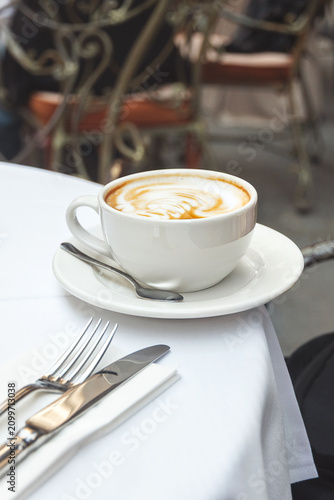 Hot cup of cappuccino on white tablecloth at restaurant