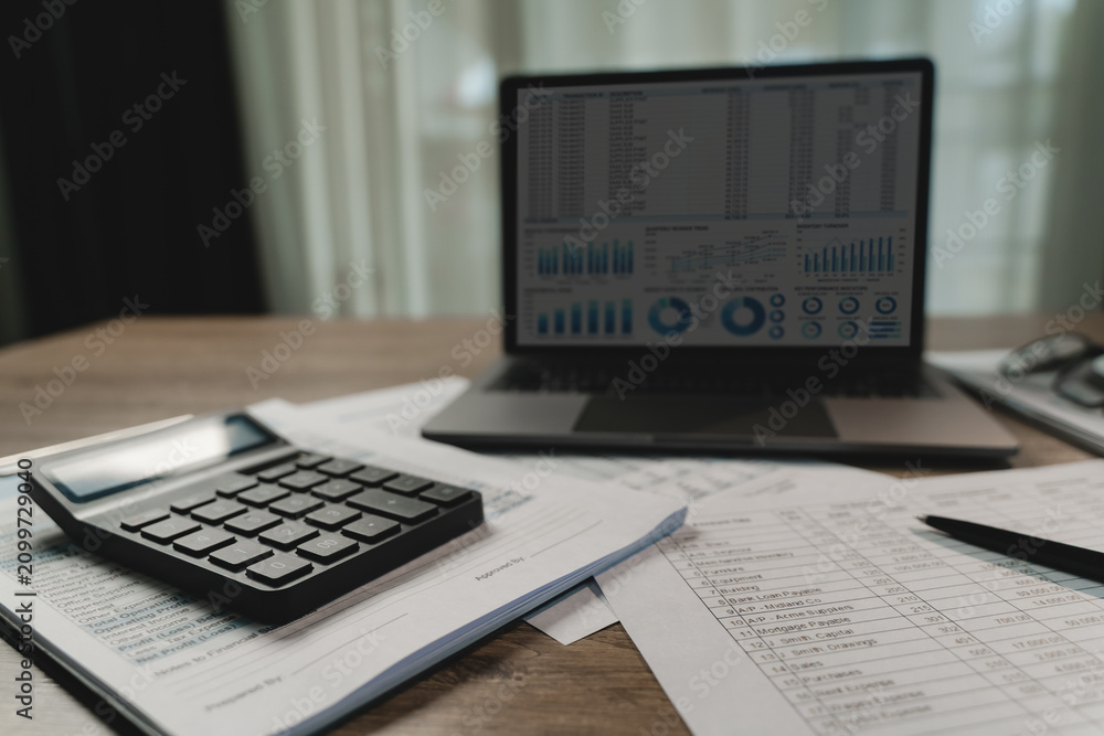 Fototapeta premium Calculator on printed financial reports beside laptop dashboard and pen on desk, showing accounting document review, budgeting workflow, and business data analysis for reporting tasks.