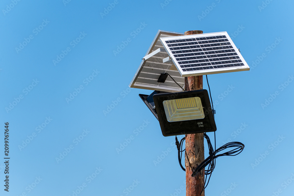Ταπετσαρία An outdoor solar-powered LED floodlight with integrated solar panels mounted on top of a rustic wooden pole