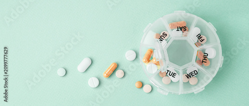 Vitamins and supplements with daily pill box on light green background, top view