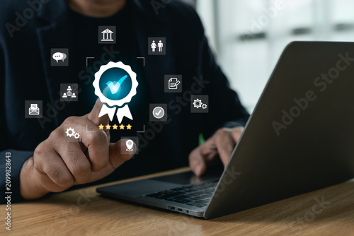 Fotografie Businessman touching a glowing certified stamp icon with five stars while working on a laptop, concept of quality assurance, customer satisfaction, and standard guarantee