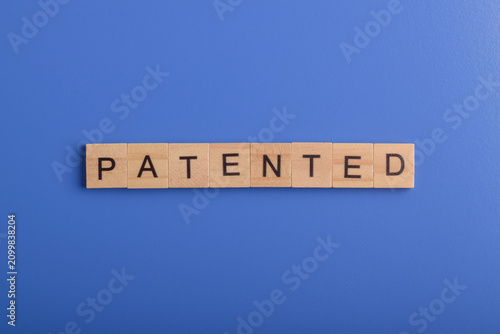 Fotografía Wooden letter blocks spelling patented on a blue background, representing intellectual property, innovation, legal protection, invention, business ownership, and exclusive rights