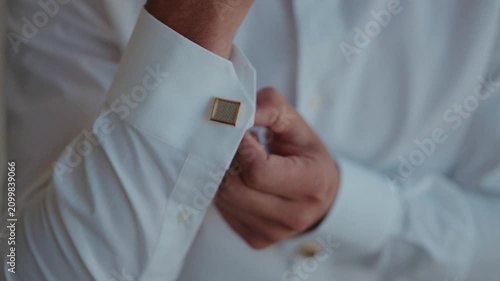 Hand fixes gold cufflink on crisp white shirt collar during formal wear preparation