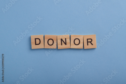 Wooden letter blocks spelling donor on a blue background, representing charitable giving, philanthropy, fundraising, financial support, nonprofit organizations, and humanitarian aid.