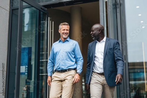 Two Businessmen Leaving Office Entrance Chatting Happily Together