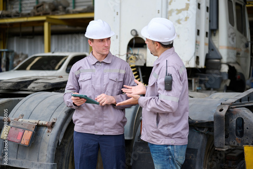Workers discussing plans near a large truck in factory