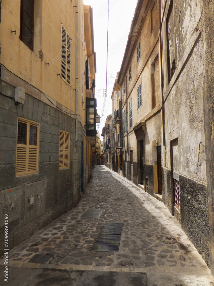Fototapeta premium Narrow historic street in Mallorca featuring traditional Mediterranean architecture and cobblestone pavement. Authentic travel destination with timeless European charm.