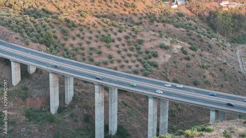 Cars drive across tall concrete viaduct spanning dry hillside terrain in Malaga Spain