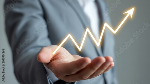 Businessman in gray suit holding glowing upward arrow showing financial success profit and corporate growth
