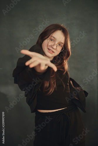 A cheerful teenage girl with long brown hair and glasses is smiling