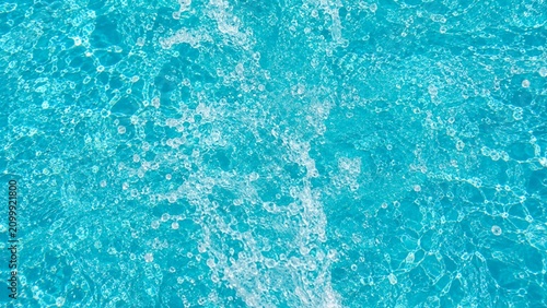 A dynamic aerial shot of splashing pool water with white foam bubbles and turquoise caustics.