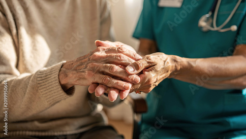 Close-up of elderly hands being held by a caregiver in teal scrubs, intimate gesture of support, concept for healthcare services, elder care and compassion advertising