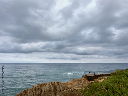 Obraz na plátně Gloomy summer morning overcast sky over coastal bluffs and safety fence overlooking the Pacific Ocean in Carlsbad, Southern California