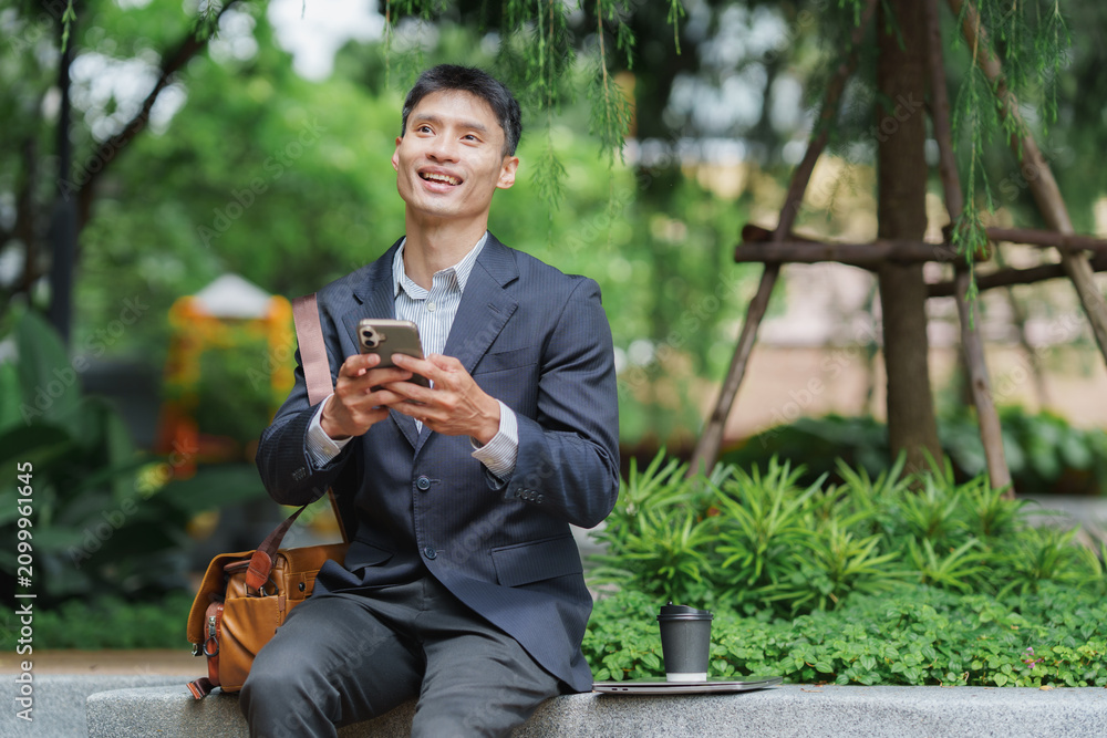 Obraz premium Asian businessman using phone and laptop outdoors