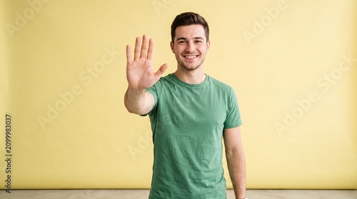 A smiling young man wearing a green t-shirt holding his hand up in a stop gesture against a ad social media download thambnail template event festive festival 2026 2027 2028