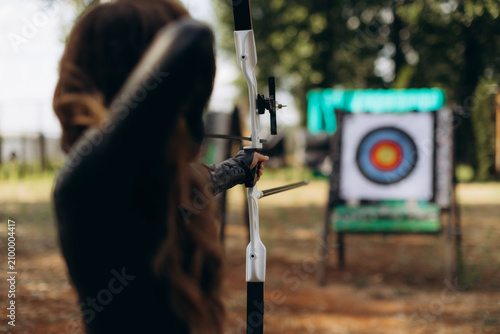 Woman targeting with bow and arrow in outdoor archery range