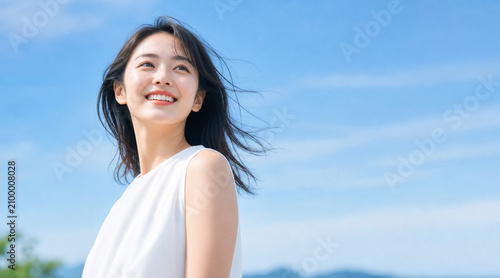 青空をバックに風に吹かれながら爽やかな笑顔を見せる若い日本人女性