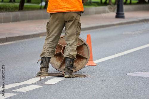 Photos Worker in uniform standing over the open sewer hatch on city street