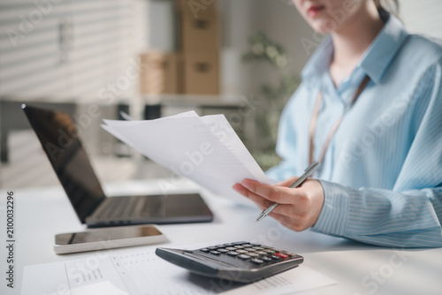 Business Professional Reviewing Invoice Documents With Laptop And Calculator In Office