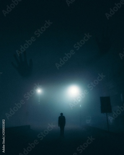 Mysterious dark silhouette of a lonely man walking in misty street at night