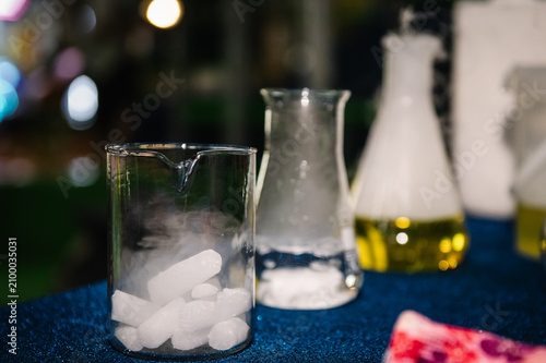 Close-up of glass laboratory beakers and flasks with dry ice pellets, water, and chemical reactions creating smoke for a children's science show.