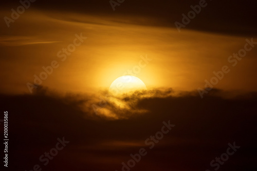 large round orange sunrise or sunset with cloudy sky for background, image shot with super telephoto lens, climate change and global warming concept