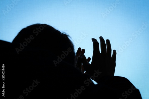 Silhouette of person raised hands in fear against blue sky for mental health awareness banner